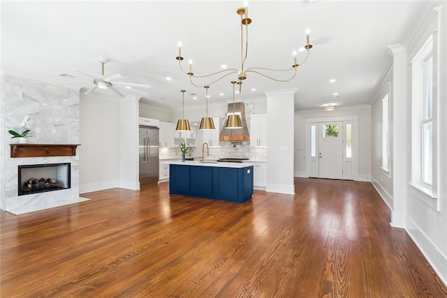 kitchen featuring wall chimney exhaust hood, stainless steel built in refrigerator, sink, blue cabinetry, and decorative light fixtures