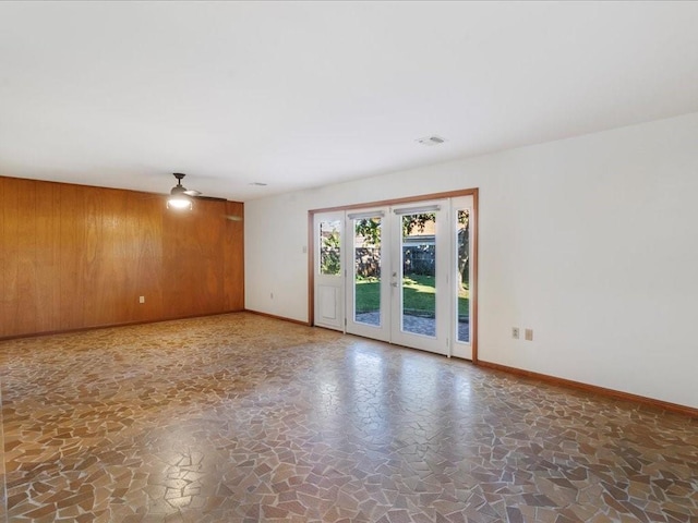 spare room featuring french doors, ceiling fan, and wooden walls