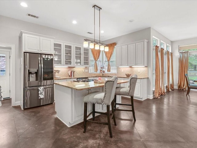 kitchen with white cabinets, stainless steel refrigerator with ice dispenser, a center island, and decorative light fixtures