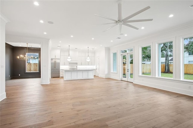 unfurnished living room featuring crown molding, ceiling fan with notable chandelier, and light wood-type flooring