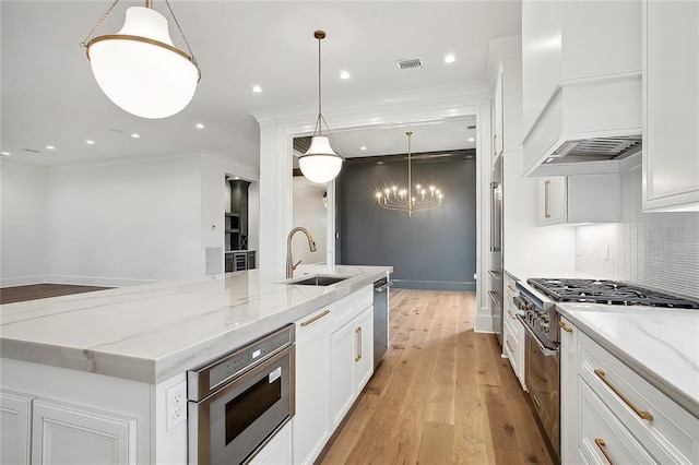 kitchen with pendant lighting, white cabinetry, sink, and light hardwood / wood-style flooring