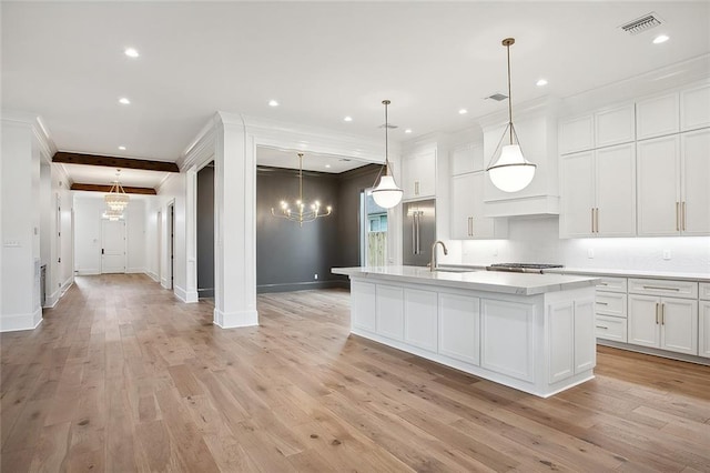 kitchen featuring decorative light fixtures, light hardwood / wood-style flooring, a center island with sink, beamed ceiling, and white cabinetry