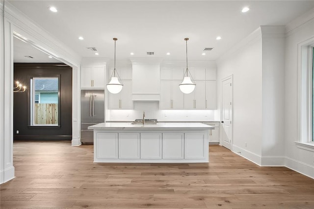 kitchen featuring a kitchen island with sink, sink, white cabinets, light hardwood / wood-style floors, and hanging light fixtures