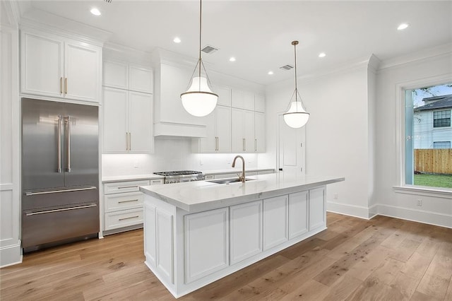 kitchen featuring white cabinetry, an island with sink, hanging light fixtures, and built in refrigerator