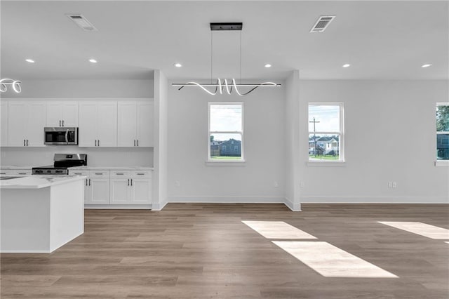 kitchen with light stone countertops, white cabinetry, hanging light fixtures, light hardwood / wood-style flooring, and appliances with stainless steel finishes