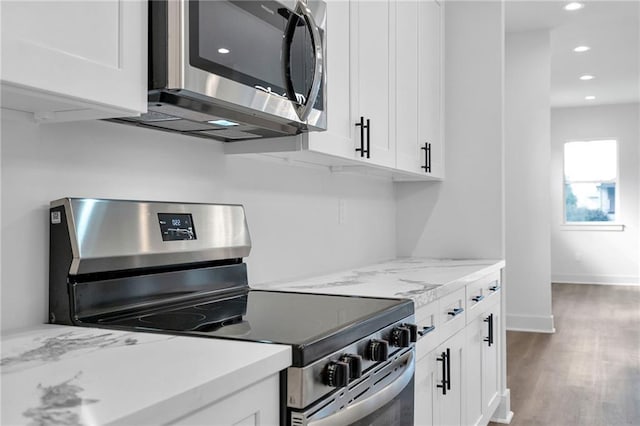 kitchen featuring white cabinets, appliances with stainless steel finishes, light stone counters, and hardwood / wood-style floors