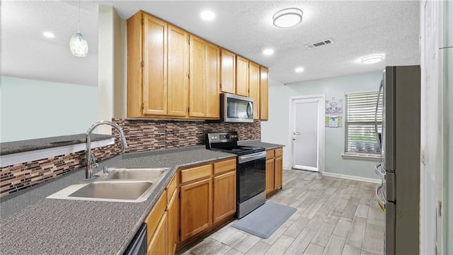 kitchen featuring decorative backsplash, stainless steel appliances, sink, light hardwood / wood-style flooring, and hanging light fixtures