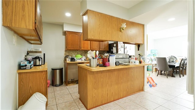 kitchen with decorative backsplash, kitchen peninsula, and light tile patterned floors