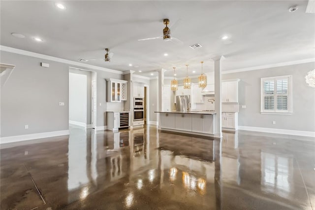 unfurnished living room featuring ceiling fan, wine cooler, crown molding, and decorative columns