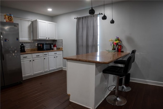 kitchen with hanging light fixtures, kitchen peninsula, dark hardwood / wood-style floors, white cabinetry, and stainless steel refrigerator