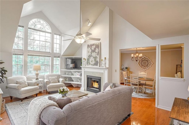 living area featuring high vaulted ceiling, ceiling fan with notable chandelier, a warm lit fireplace, and wood finished floors