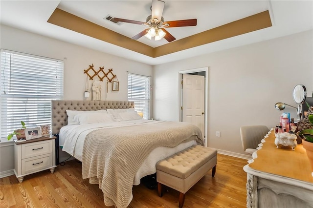 bedroom featuring a tray ceiling, multiple windows, and light wood-type flooring