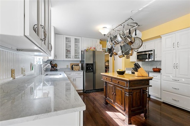 kitchen with light stone counters, appliances with stainless steel finishes, glass insert cabinets, dark wood-type flooring, and a sink