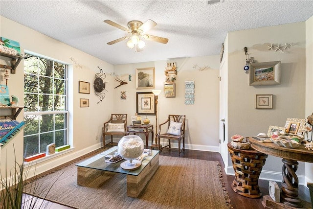 living area featuring a textured ceiling, baseboards, dark wood finished floors, and a ceiling fan