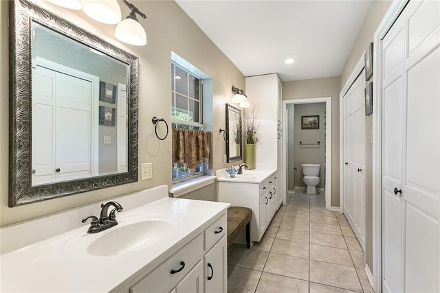 full bath featuring two vanities, tile patterned flooring, a sink, and toilet