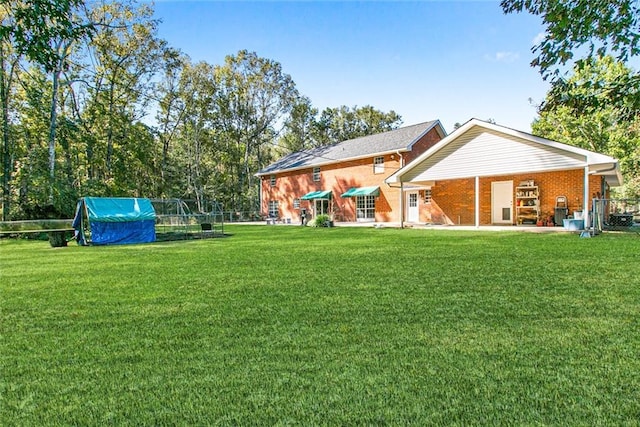 rear view of property with brick siding, a lawn, an outdoor structure, and fence