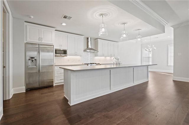 kitchen with built in appliances, pendant lighting, white cabinets, and wall chimney range hood