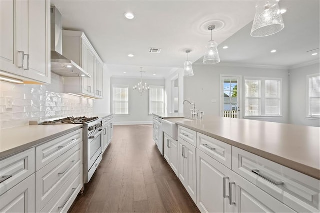 kitchen with sink, wall chimney range hood, pendant lighting, high end stainless steel range, and white cabinets