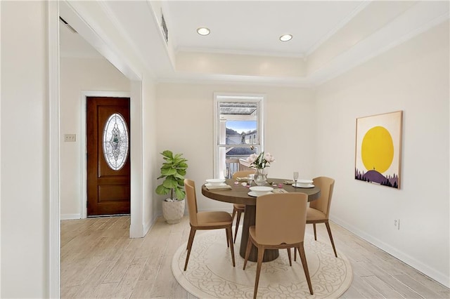 dining room with light hardwood / wood-style floors, ornamental molding, and a tray ceiling