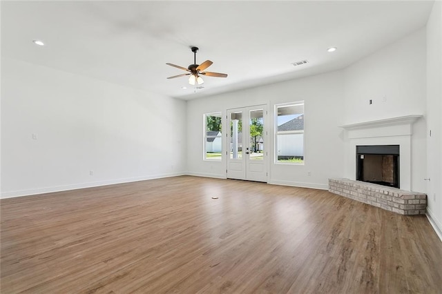 unfurnished living room featuring a fireplace, light hardwood / wood-style floors, french doors, and ceiling fan