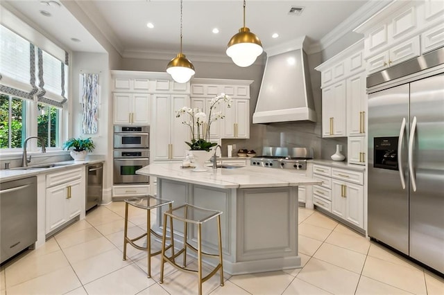 kitchen featuring custom range hood, stainless steel appliances, sink, decorative light fixtures, and a center island with sink