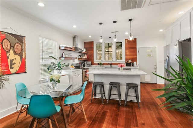 kitchen with wall chimney exhaust hood, dark hardwood / wood-style flooring, decorative light fixtures, a kitchen island, and appliances with stainless steel finishes