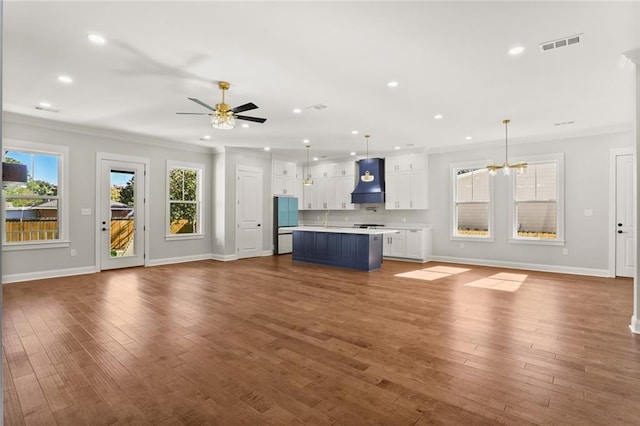 unfurnished living room with crown molding, sink, ceiling fan with notable chandelier, and hardwood / wood-style flooring