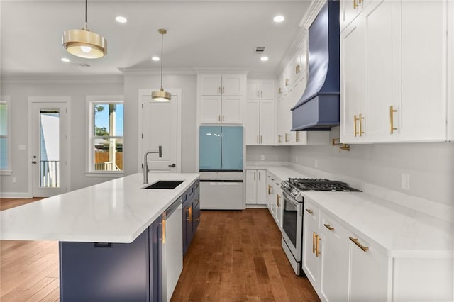 kitchen featuring appliances with stainless steel finishes, custom range hood, a kitchen island with sink, sink, and hanging light fixtures