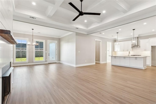 unfurnished living room with sink, coffered ceiling, beamed ceiling, light hardwood / wood-style floors, and ceiling fan with notable chandelier