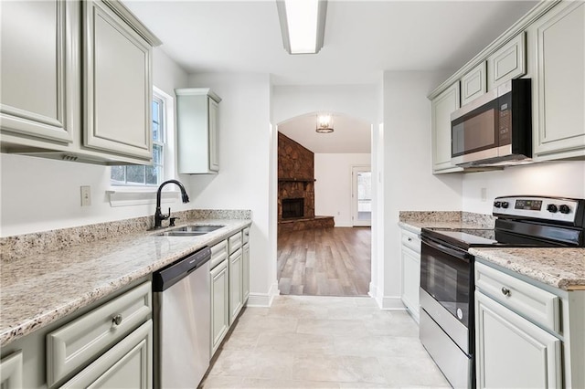 kitchen with sink, a stone fireplace, stainless steel appliances, and light stone countertops