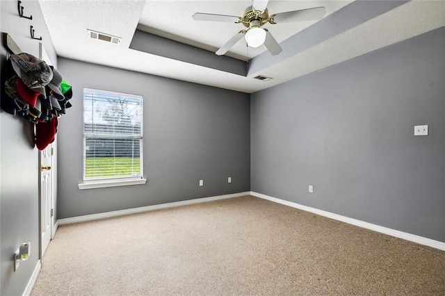 empty room with carpet floors, a tray ceiling, and ceiling fan