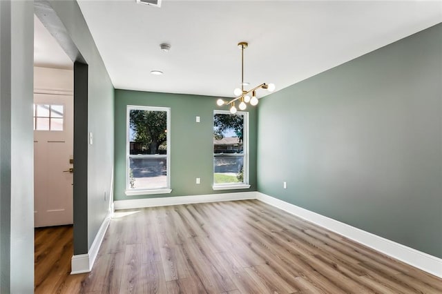 unfurnished dining area featuring a healthy amount of sunlight, a notable chandelier, and light hardwood / wood-style floors