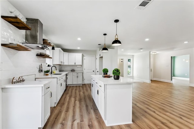 kitchen with pendant lighting, a center island, white cabinets, wall chimney range hood, and light hardwood / wood-style flooring