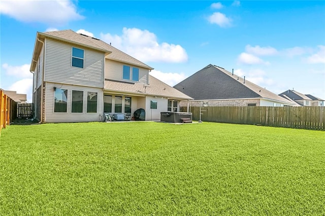 rear view of house with a hot tub and a lawn