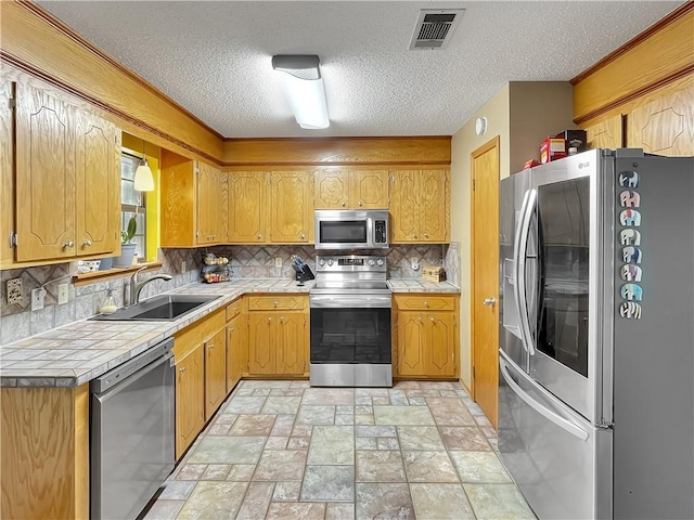 kitchen with sink, decorative backsplash, a textured ceiling, appliances with stainless steel finishes, and tile counters