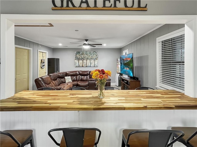 kitchen with a breakfast bar area, ceiling fan, wooden walls, and ornamental molding