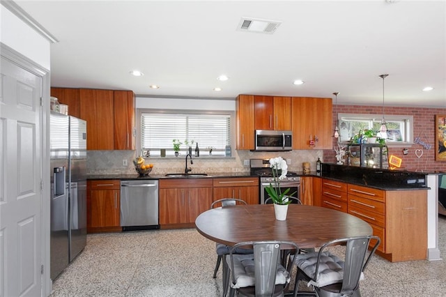 kitchen with sink, hanging light fixtures, dark stone counters, decorative backsplash, and appliances with stainless steel finishes