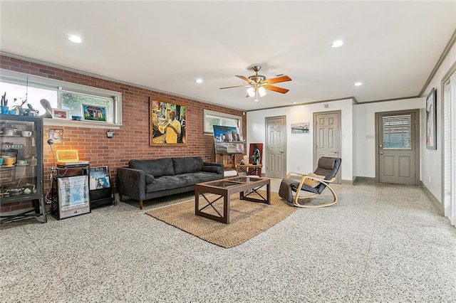 living room featuring ceiling fan, ornamental molding, and brick wall