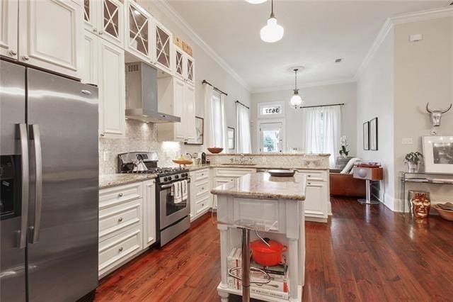 kitchen featuring appliances with stainless steel finishes, light stone counters, ornamental molding, wall chimney exhaust hood, and hanging light fixtures