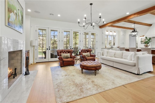 living room with beamed ceiling, french doors, a chandelier, and light hardwood / wood-style flooring