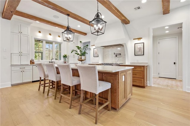 kitchen featuring a large island, light hardwood / wood-style flooring, white cabinets, and decorative light fixtures