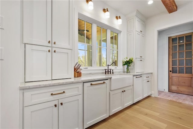 bar with light stone counters, sink, white cabinets, and light hardwood / wood-style floors