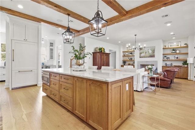 kitchen with light stone counters, light hardwood / wood-style flooring, beamed ceiling, a center island, and hanging light fixtures