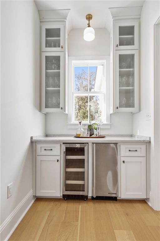 bar with stainless steel fridge, white cabinets, beverage cooler, and light hardwood / wood-style floors