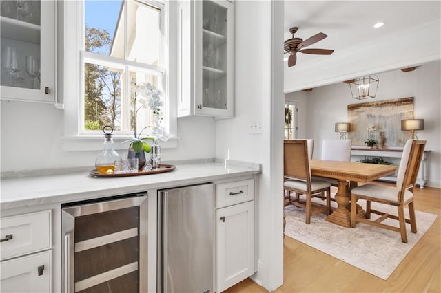 bar featuring stainless steel fridge, light wood-type flooring, beverage cooler, ceiling fan, and white cabinets