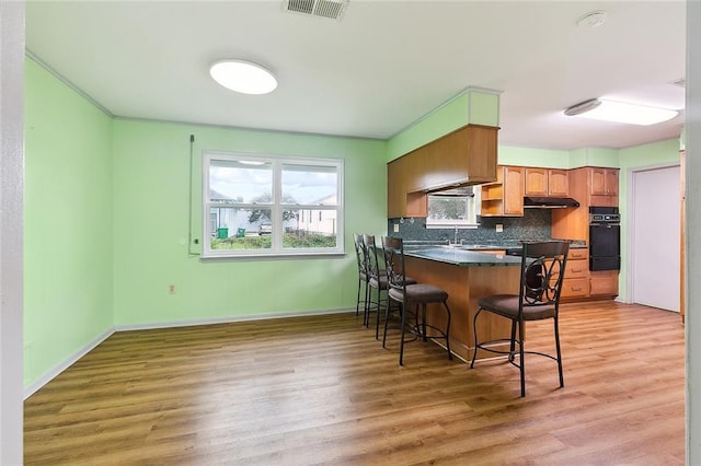 kitchen with a breakfast bar area, black oven, hardwood / wood-style floors, and kitchen peninsula