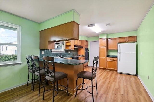 kitchen with crown molding, sink, light hardwood / wood-style floors, tasteful backsplash, and white fridge