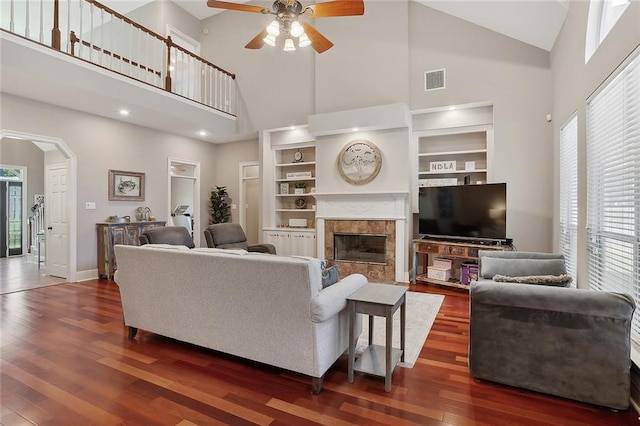 living room featuring a tiled fireplace, dark hardwood / wood-style floors, built in features, and ceiling fan