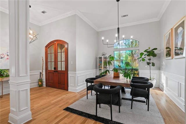 dining area featuring decorative columns, crown molding, an inviting chandelier, and light wood-type flooring