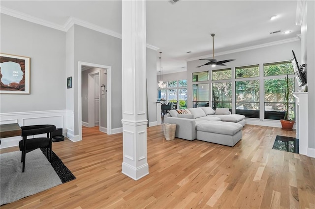 living room featuring ceiling fan with notable chandelier, light wood-type flooring, ornate columns, and ornamental molding